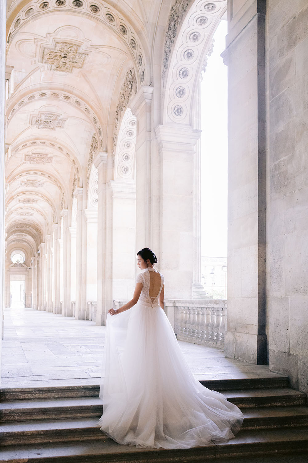 A bride is in the louvre and holds her wedding dress in her hands